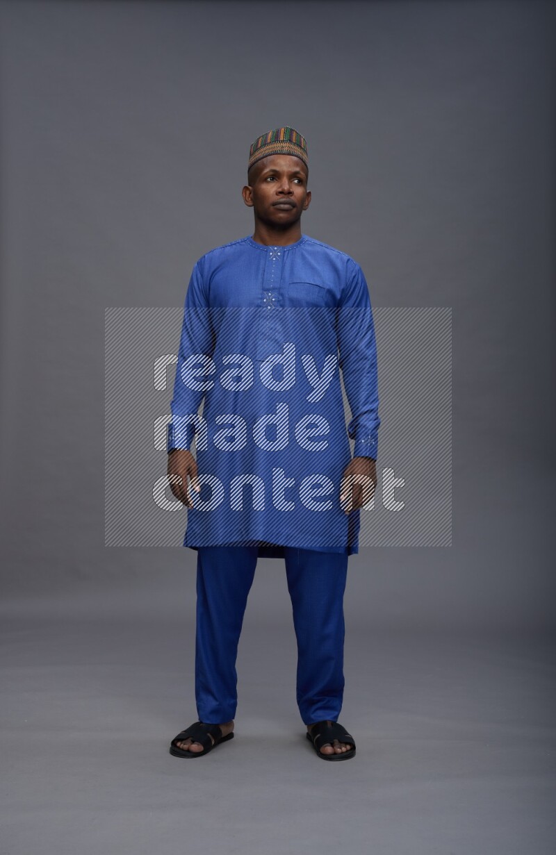 Man wearing Nigerian outfit standing interacting with the camera on gray background