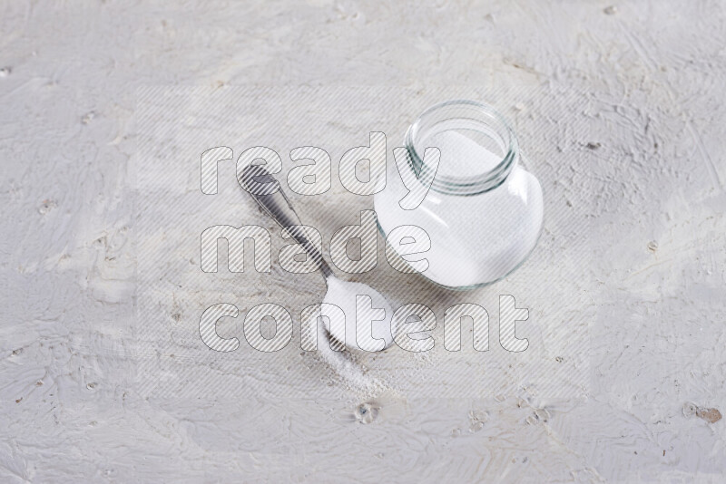 A glass jar full of fine table salt on white background