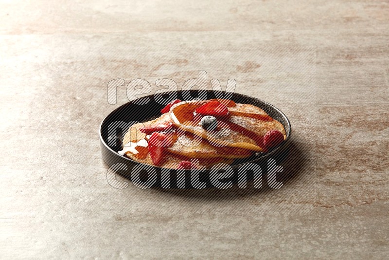 Three stacked mixed berries pancakes in a black plate on beige background