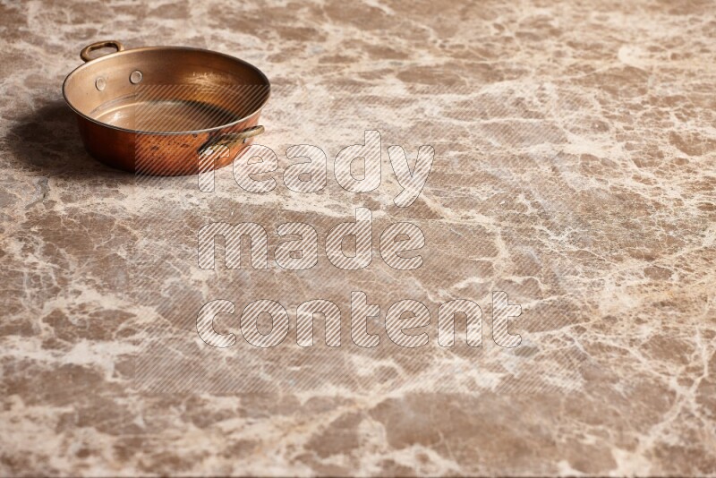 A small copper pan on beige marble background