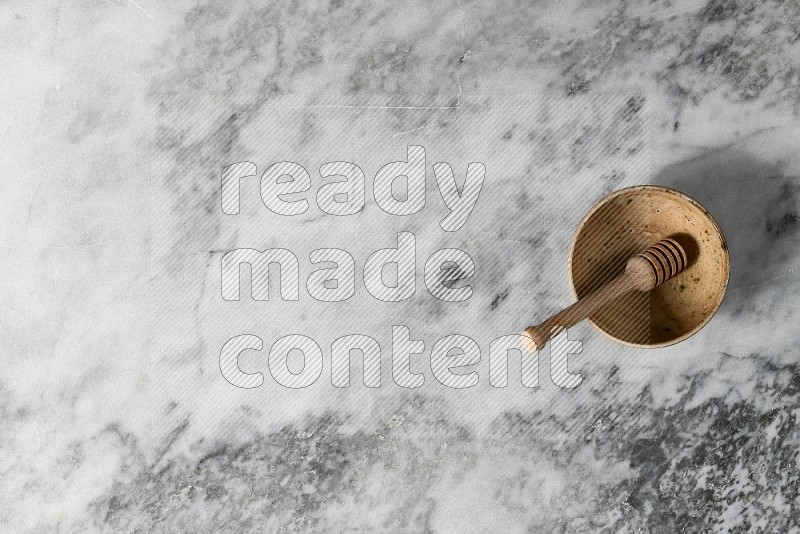 Beige Pottery Bowl with wooden honey handle in it, on grey marble flooring, Top View