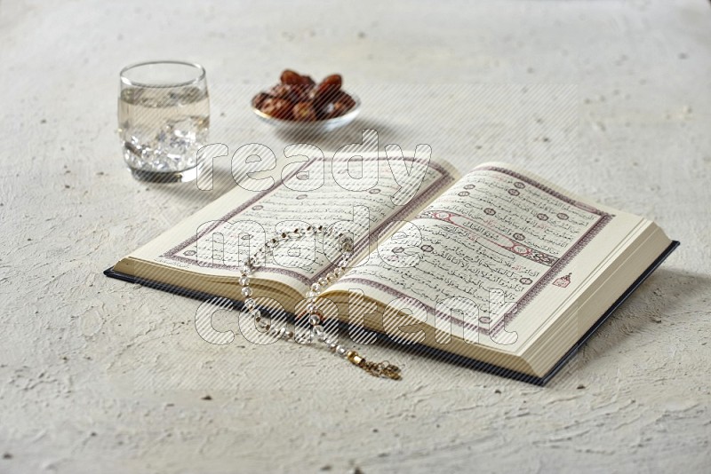 Quran with dates, prayer beads and different drinks on textured white background