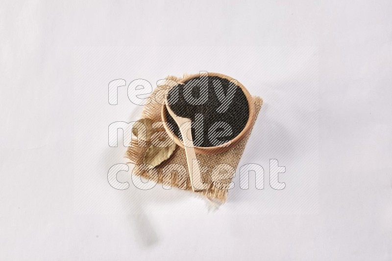 A wooden bowl and wooden spoon full of black seeds on a piece of burlap on a white flooring