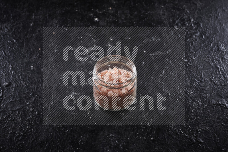 A glass jar full of coarse himalayan salt crystals on black background