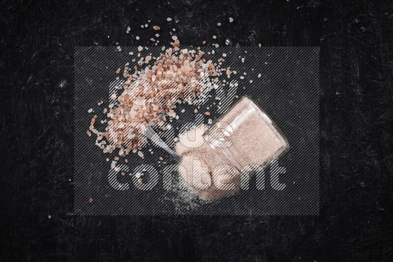 A glass jar full of fine himalayan salt with some himalayan crystals beside it on a black background