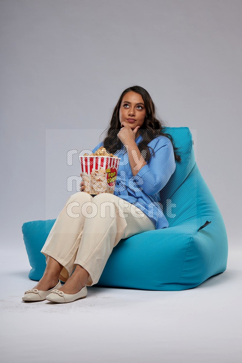 A woman sitting on a blue beanbag and eating popcorn