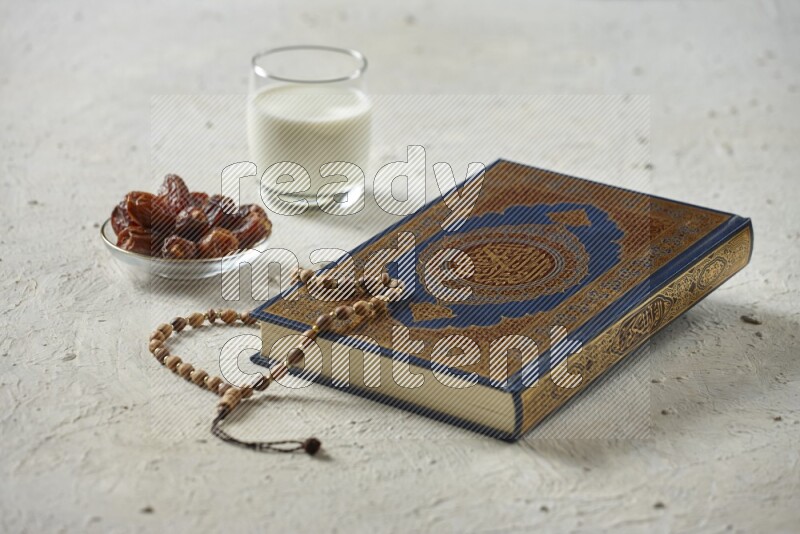 Quran with dates, prayer beads and different drinks all placed on textured white background