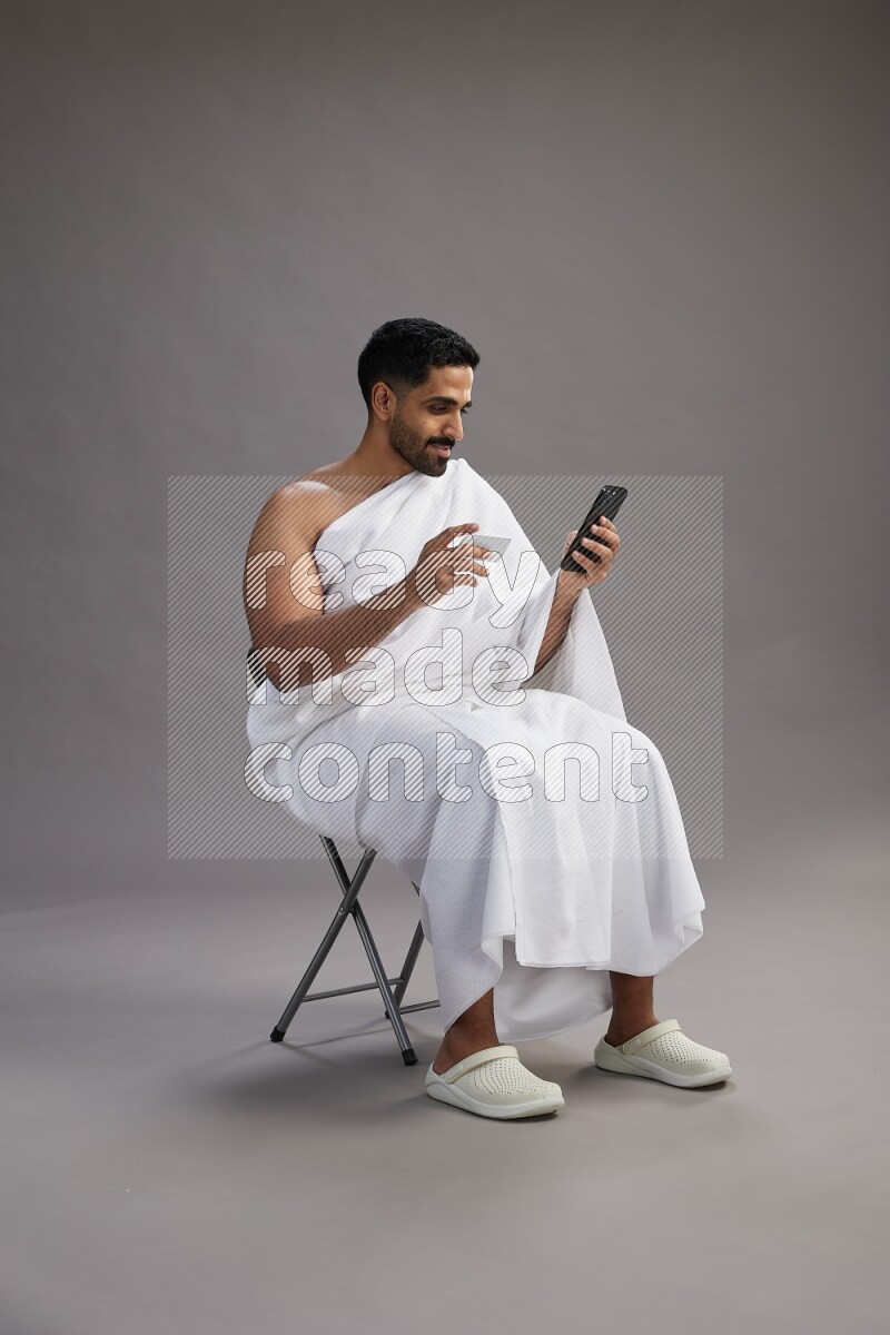 A man wearing Ehram sitting on chair holding ATM card on gray background