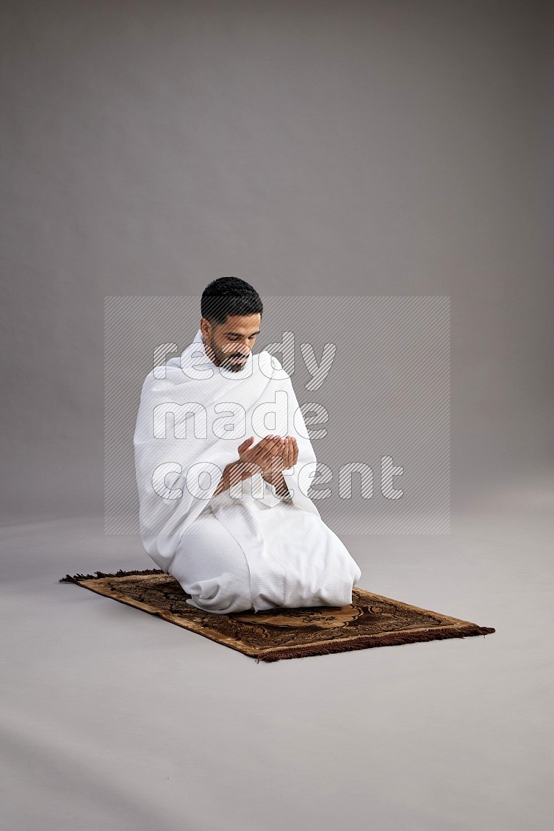 A man wearing Ehram performing dua'a on gray background