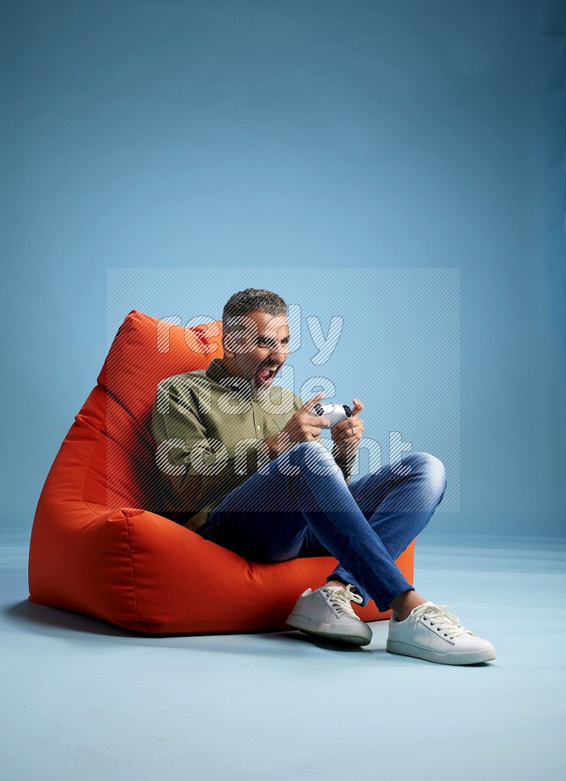A man sitting on an orange beanbag and gaming with joystick