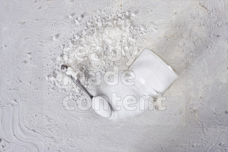 A glass jar full of table salt with some sea salt crystals beside it on a white background