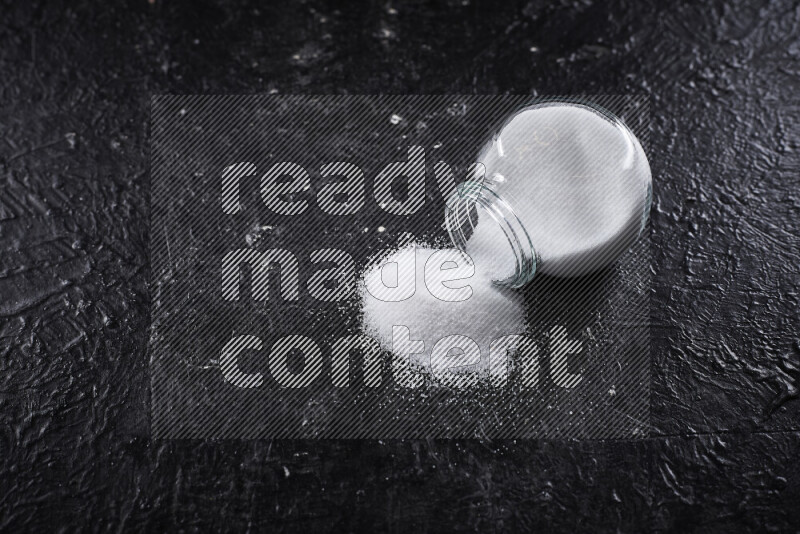 A glass jar full of fine table salt on black background