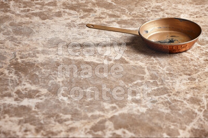 A small copper pan on beige marble background