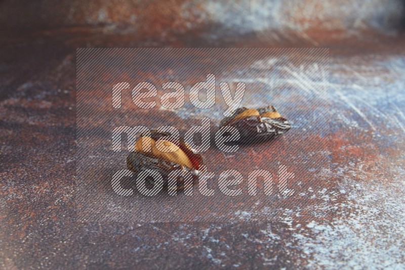 two almond stuffed madjoul dates on a rustic reddish background