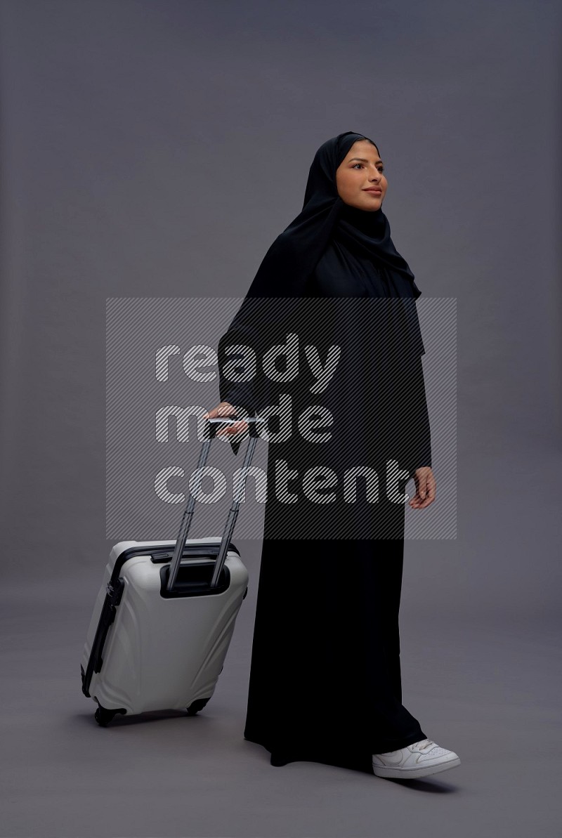 Saudi woman wearing Abaya standing holding bag on gray background