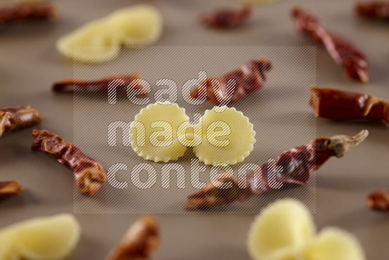 Raw pasta with different ingredients such as cherry tomatoes, garlic, onions, red chilis, black pepper, white pepper, bay laurel leaves, rosemary and cardamom on beige background