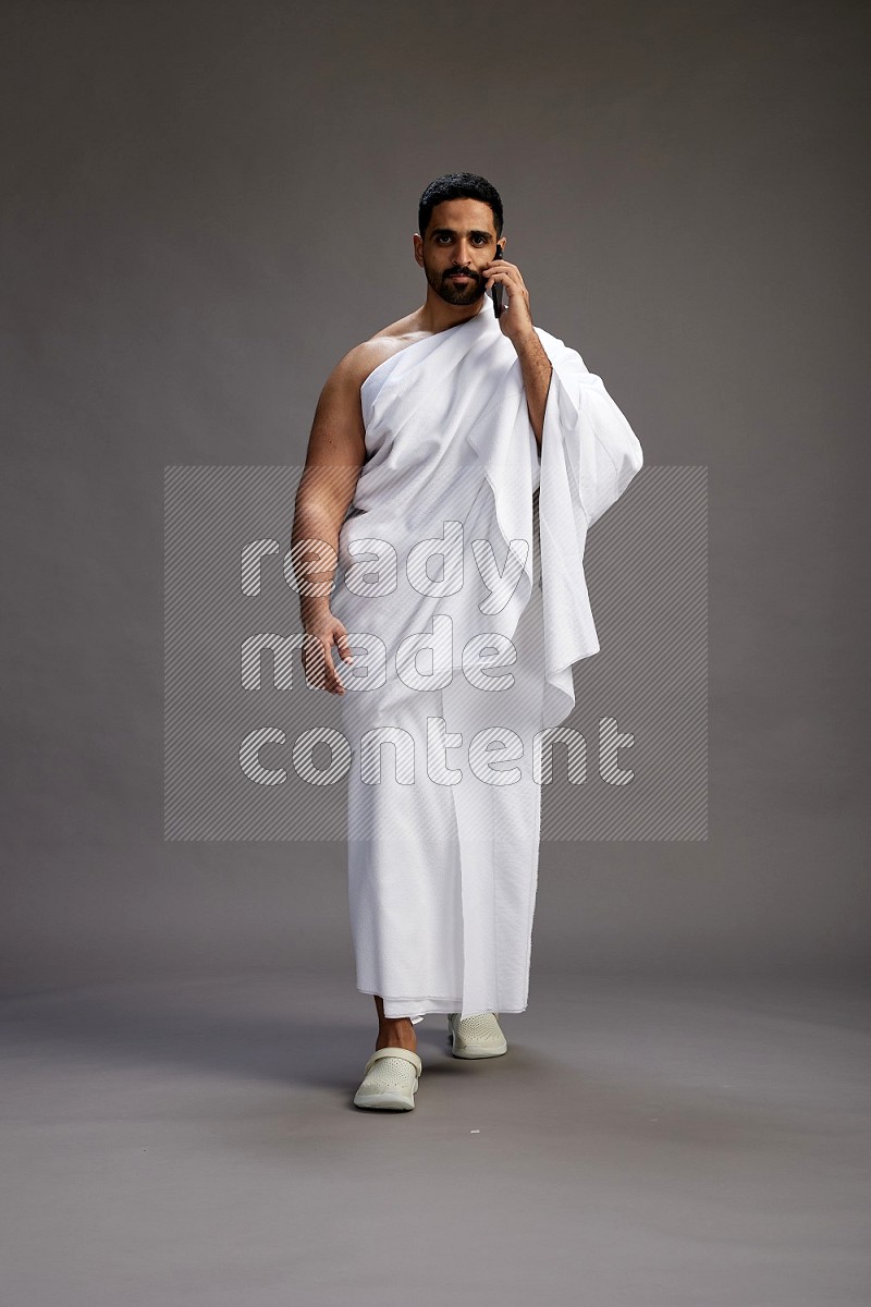 A man wearing Ehram Standing talking on phone on gray background