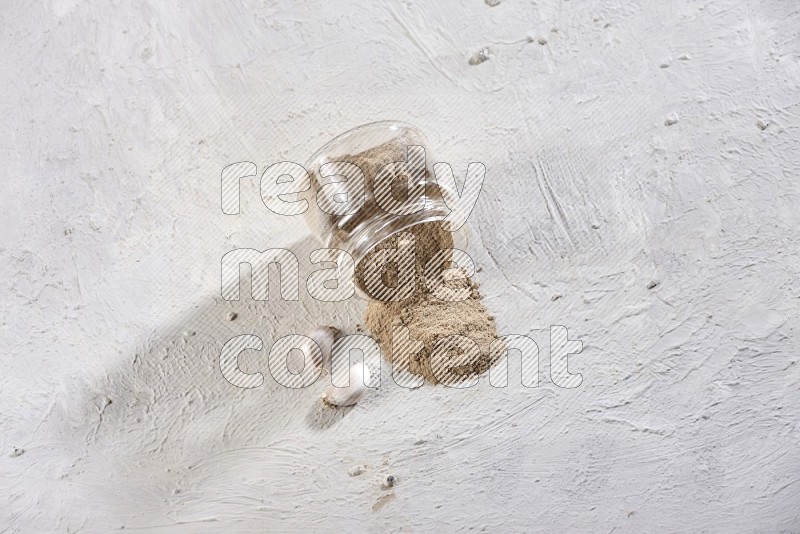 A glass jar full of garlic powder flipped and the powder came out on a textured white flooring in different angles