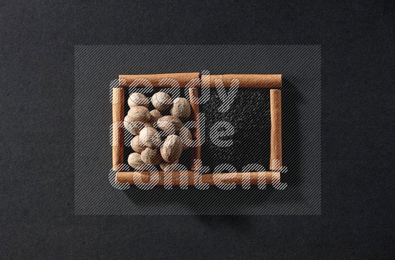 2 squares of cinnamon sticks full of black seeds and nutmeg on black flooring