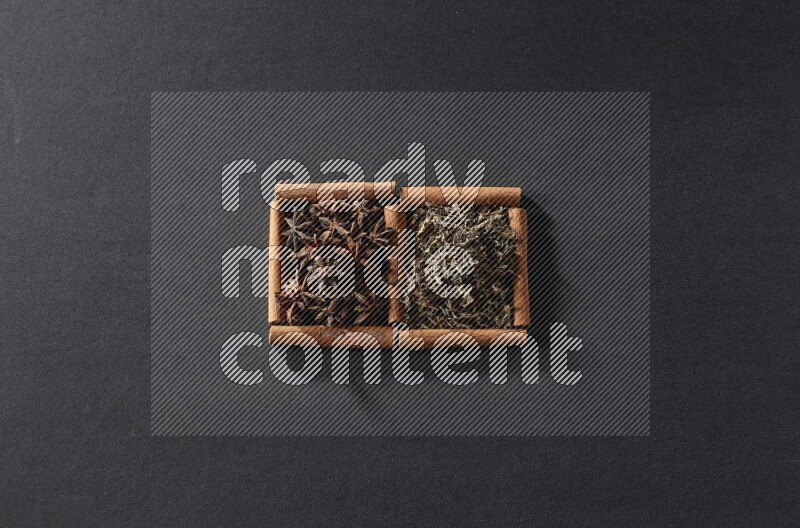 مربعان من أعواد القرفة ممتلئان باليانسون النجمي والريحان المجفف علي خلفية سوداء