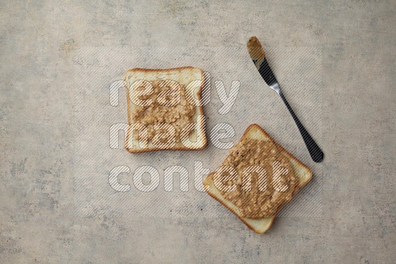 Crunchy  peanut butter on a toasted white toast slices with a spreading knife on a light blue textured background
