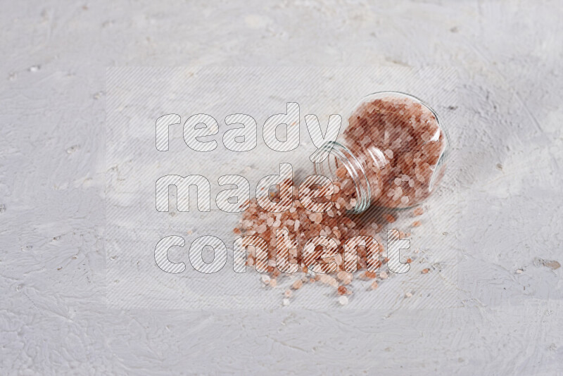 A glass jar full of coarse himalayan salt crystals on white background