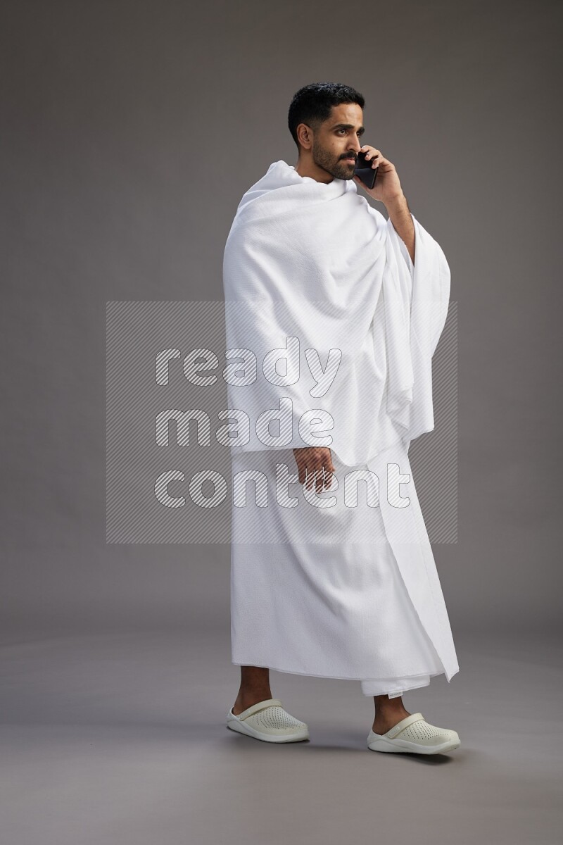 A man wearing Ehram Standing talking on phone on gray background
