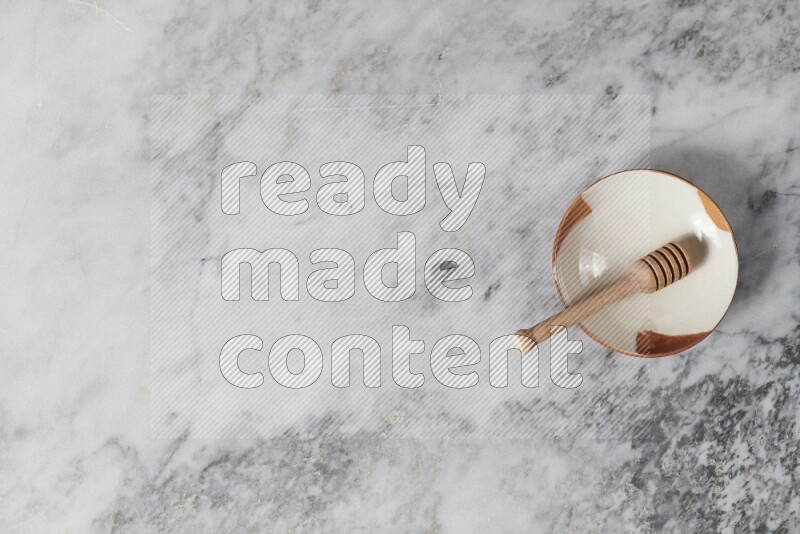 Multicolored pottery plate with wooden honey dipper in it on grey marble background