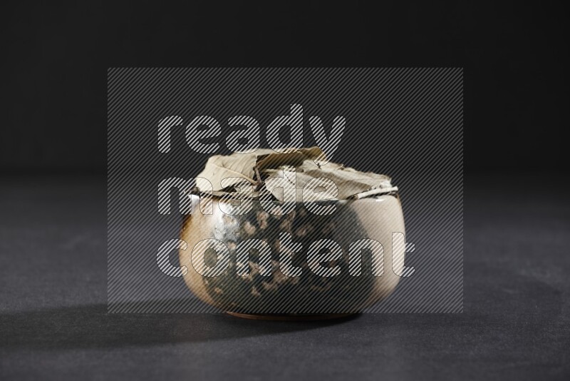 وعاء فخاري متعدد الألوان ممتلئ بأوراق الغار المجففة على أرضية سوداء