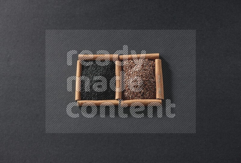 مربعان من أعواد القرفة ممتلئان ببذور الكتان وحبة البركة السوداء علي خلفية سوداء