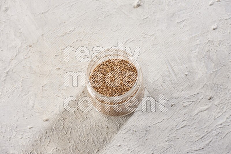A glass jar full of mustard seeds on a textured white flooring