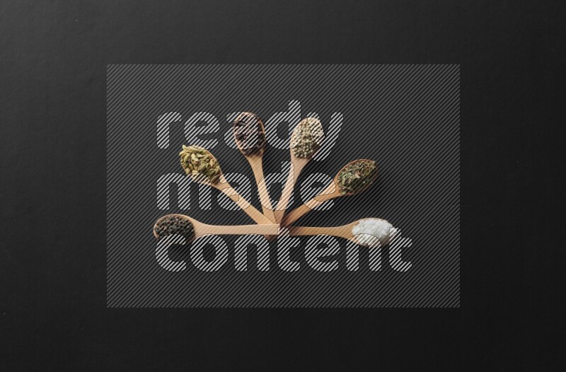 الفلفل الأبيض والقرنفل والهيل والملح والفلفل الأسود وريحان مجفف في معالق خشبية علي خلفية سوداء