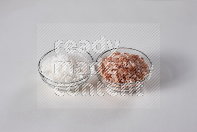 2 glass bowls one is filled with himalayan salt and the other with white salt on white background