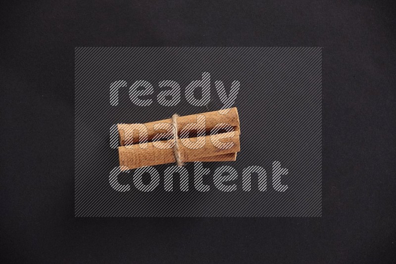 4 Cinnamon sticks stacked and bounded on black flooring