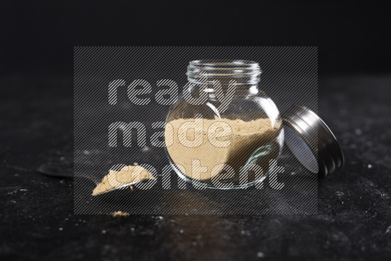 A glass jar full of ground ginger powder on black background