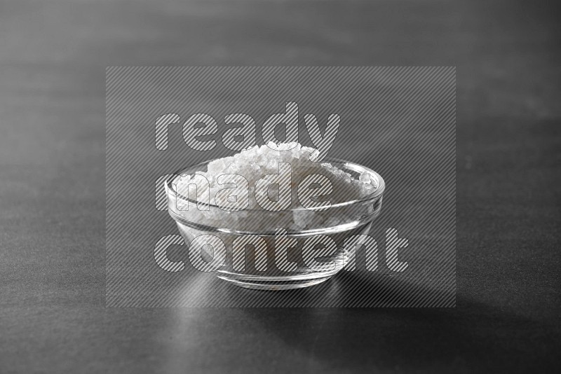 A glass bowl full of salt on black flooring