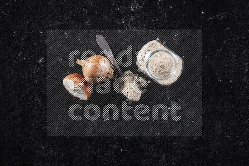 A glass jar full of onion powder on black background