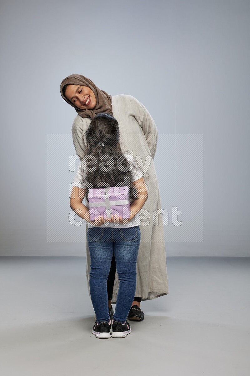 A girl standing hiding a gift behind her back for her mother on gray background