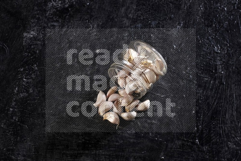 A glass jar full of garlic cloves flipped and the cloves came out on a textured black flooring in different angles