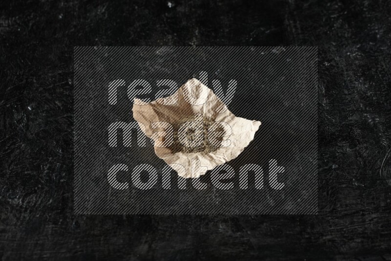 Cardamom powder in a crumpled piece of paper on textured black flooring