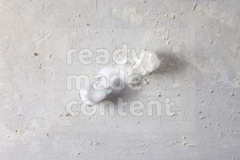 2 glass jars one is filled with table salt and the other with coarse sea salt on white background