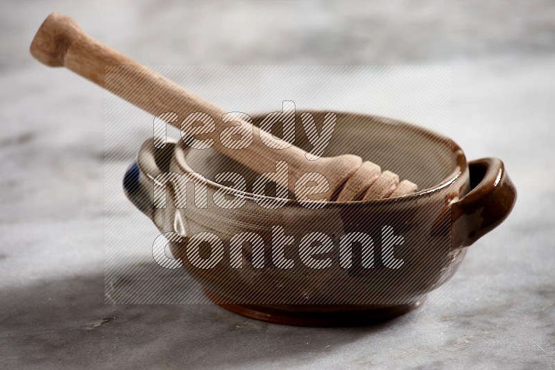 Multicolored Pottery bowl with wooden honey handle in it, on grey marble flooring, 15 degree angle
