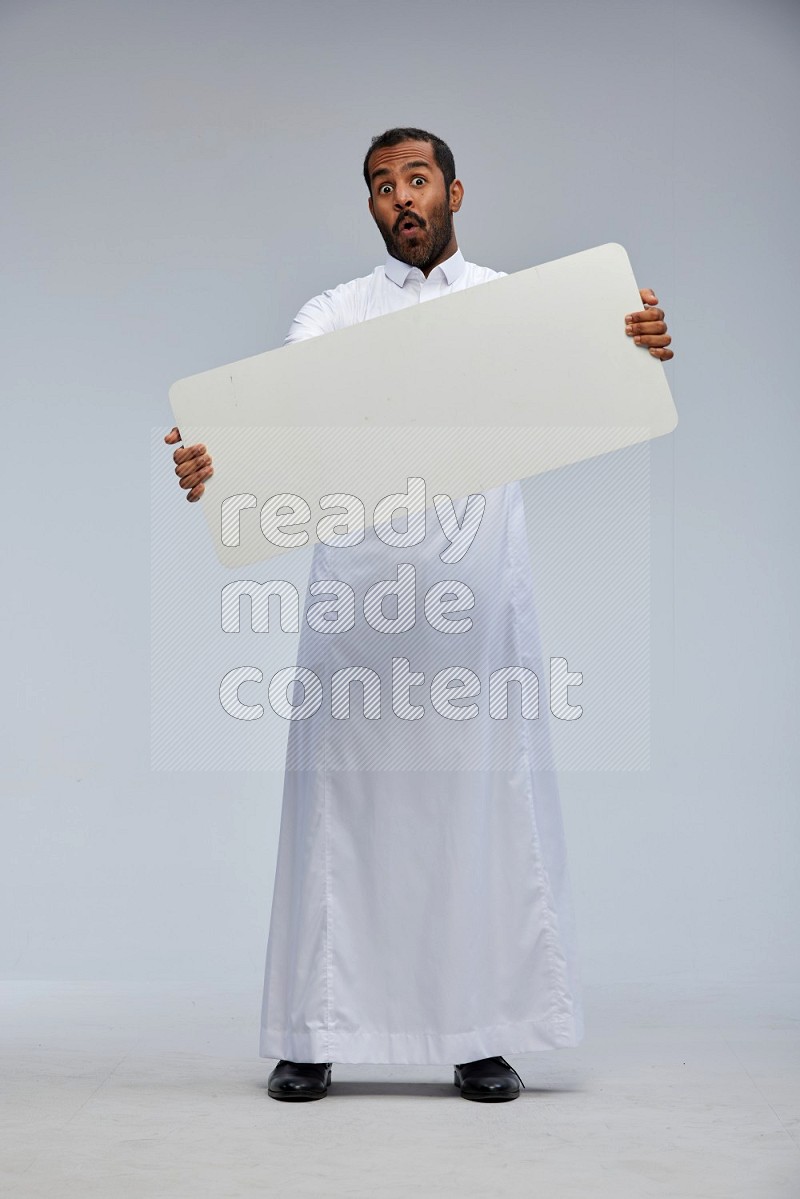 Saudi man wearing Thob standing holding board on Gray background