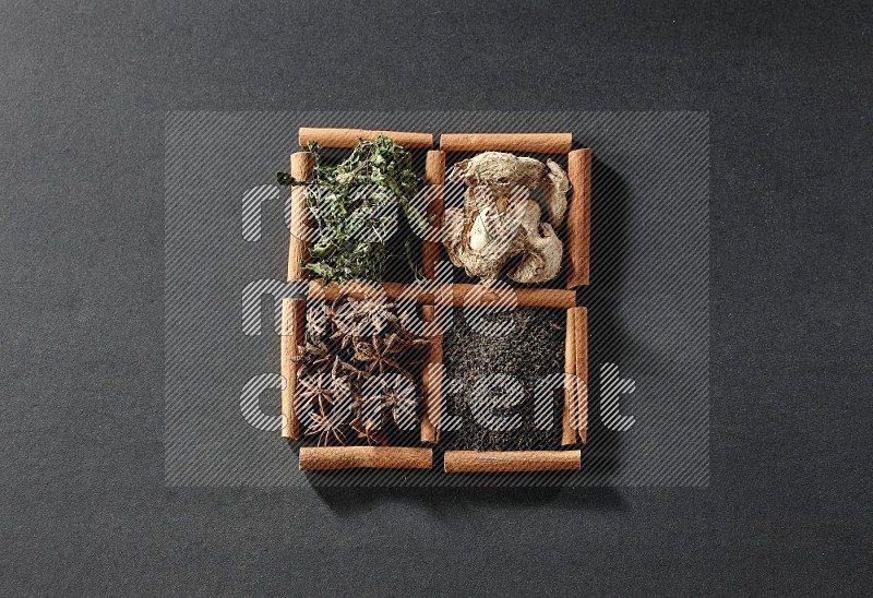 4 squares of cinnamon sticks full of black tea, dried ginger, dried mint leaves and star anise on black flooring