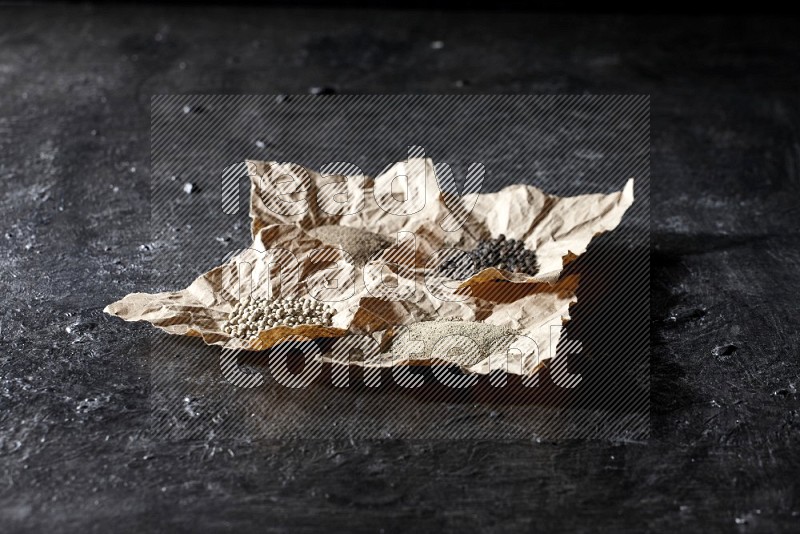 Crumpled pieces of paper full of black and white pepper beads and powder on a textured black flooring