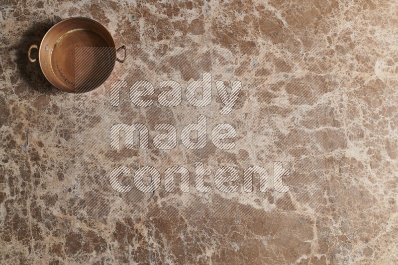 A small copper pan on beige marble background