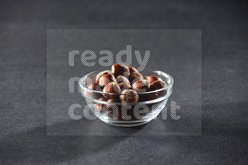 A glass bowl full of hazelnuts on a black background in different angles