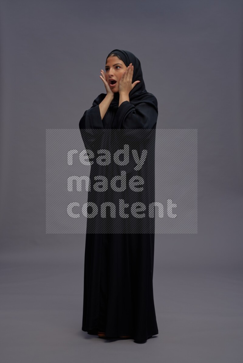 Saudi woman wearing Abaya standing hands behind head on gray background