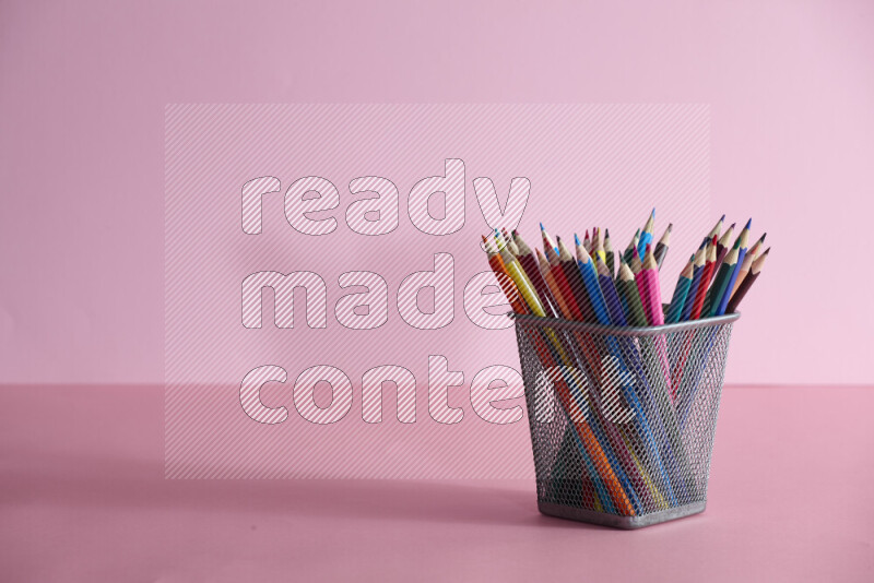 Pens, pencils and other different school supplies in a metal pen holder on rose background