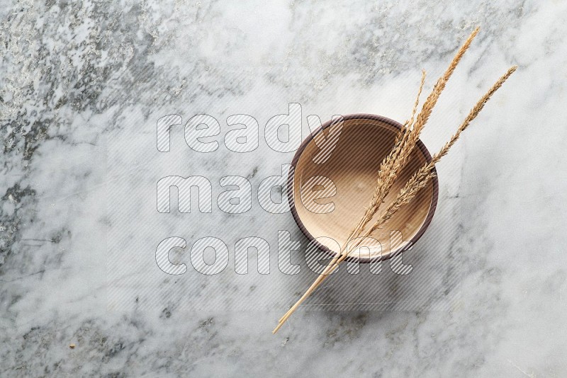 Wheat stalks on Beige Pottery Oven Bowl Plate on grey marble flooring, Top view
